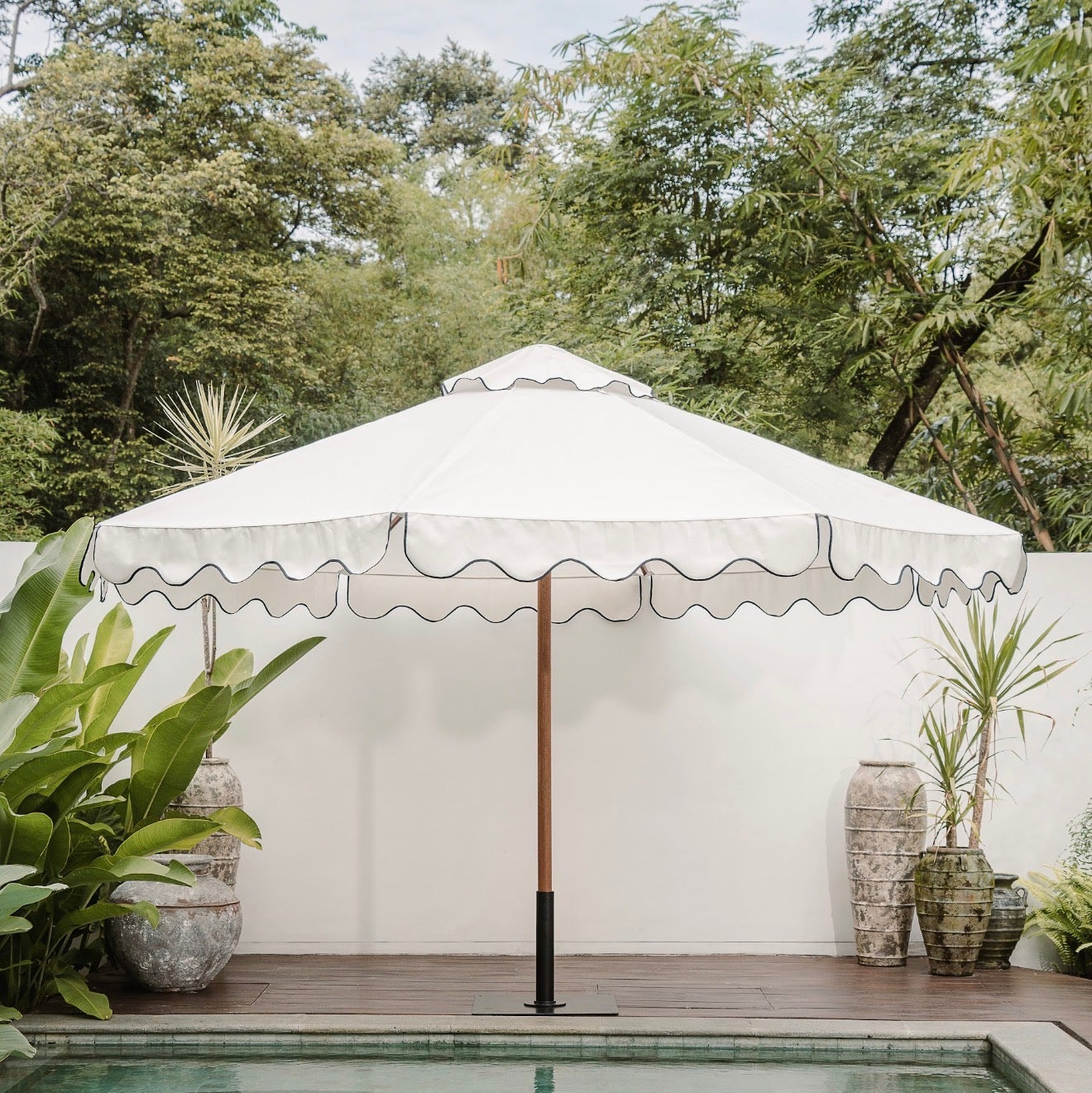 Large outdoor umbrella over a pool with greenery and a white wall in the background