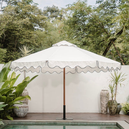 Large outdoor umbrella over a pool with greenery and a white wall in the background