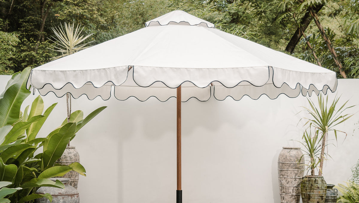 White scalloped-edge timber market umbrella with black trim in a garden setting